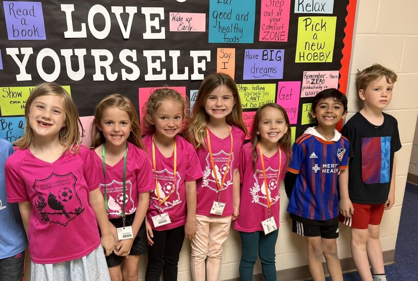 Students wear sports jerseys in front of a bulletin board that reads "love yourself"